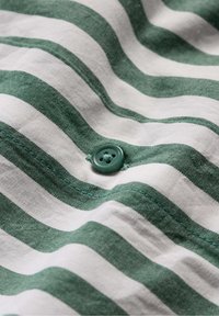 Tessuto a righe verdi e bianche con una finitura testurizzata, caratterizzato da un singolo bottone verde e cuciture visibili lungo il bordo.
