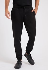 Schwarze Jogginghosen aus weichem Material, mit einem elastischen Bund und Kordelzug, Seitentaschen und schmal zulaufenden Bündchen.