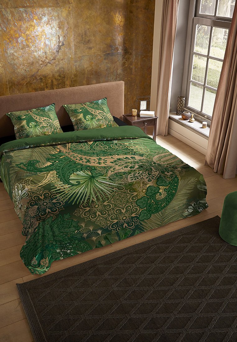 Letto matrimoniale con biancheria da letto a motivi verdi e cuscini coordinati, testiera in stoffa marrone, pavimento in legno, tavolino, grande finestra, tende beige.