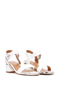 Sandalias blancas de tacón cuadrado con dos correas anchas. Material sintético suave, hebilla ajustable en el tobillo y un acento plateado en la punta.