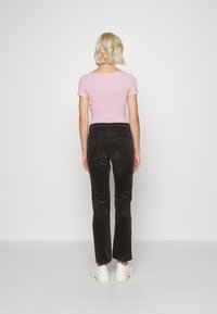Chemise rose ajustée avec des manches ruffles, associée à un pantalon en velours côtelé marron. Des baskets blanches complètent la tenue. Vue de dos.
