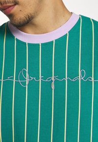 Green striped T-shirt with lavender crew neckline, featuring yellow and white vertical stripes and embroidered "Originals" in white thread.