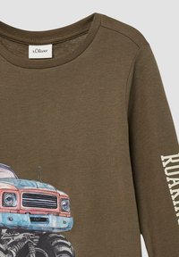 Olivgrünes Langarmhemd mit einem Grafiken eines blauen und rosa Vintage-Trucks mit übergroßen Reifen sowie dem weißen Schriftzug "ROARING" auf dem Ärmel.
