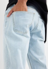 Jeans de mezclilla azul claro con un corte relajado, que cuentan con bolsillos traseros, costuras visibles en un color contrastante y una textura suave.