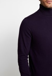Dunkellilan Rollkragenpullover aus weichem Material. Figurbetontes Design mit langen Ärmeln und hohem Kragen. Nahtlose Stricktextur.