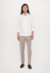 Weißes Langarmhemd mit Knopfleiste, beige maßgeschneiderte Hose und dunkle Slipper; glattes Material mit minimalistischem Design und klaren Linien.