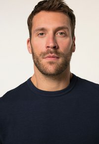 Námořnická modrá tričko s kulatým výstřihem, vyrobené z měkké, texturované tkaniny, s jemným nerovnoměrným vzorem a minimálními designovými detaily.