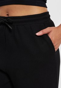 Black ribbed pants featuring a drawstring waist and side pockets. The fabric texture is soft, with vertical lines creating a subtle pattern.