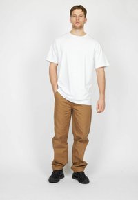 White short-sleeved t-shirt paired with loose khaki trousers and black athletic shoes. Simple design, smooth texture, with a relaxed fit.