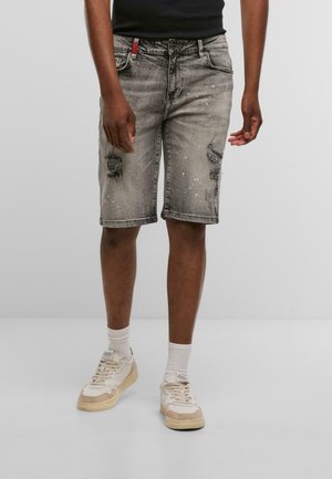 Pantalones cortos de mezclilla gris con detalles desgastados, bolsillos frontales y un ajuste regular. Combinados con zapatillas ligeras y calcetines blancos.