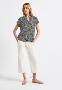 Top a maniche corte bianco e nero con scollatura a V, abbinato a pantaloni a gamba larga crema e sandali leggeri tan con cinturini.