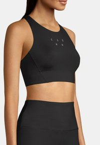 Svart sport-BH med høy hals og racerback-design. Har små trykte tekster i et rutenettmønster foran. Glatt tekstur.