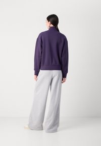 Paarse oversized sweatshirt met hoge kraag, gecombineerd met lichtgrijze wijde joggingbroek. Zachte textuur, casual pasvorm en elastische manchetten.