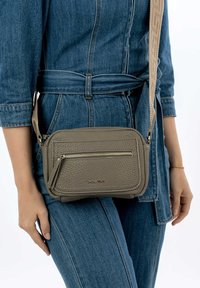 Sac bandoulière synthétique gris avec une surface texturée, présentant une poche zippée à l'avant et une sangle ajustable à motifs.