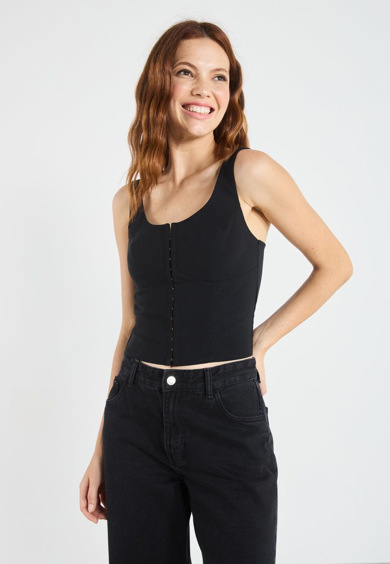Mustmust crop-top, mille ümmargune kaelus ja esine nup Closure; valmistatud siledast kangast, millel on minimaalne tekstuur ja keha lähedane disain.