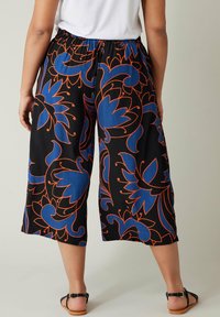 Svarta vida byxor med stora blå blommönster i orange konturer. Elastisk midja, kort längd och slät tygtextur.