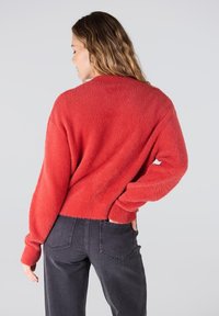 Rode fluffy trui met lange mouwen, cropped ontwerp en een textuurafwerking. Gecombineerd met donkergrijze high-waisted jeans.