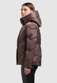 Bruine donsjas met een hoge kraag, ruitgestikt patroon en logodetail op de mouw. Waterafstotend materiaal en gladde textuur.