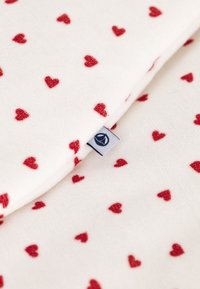 Fleece dekentje in het wit met verspreide rode hartmotieven. Heeft een blauw label aan de rand. Zachte textuur. Compact ontwerp.