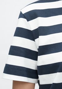 Camiseta de manga corta a rayas en azul marino y blanco, confeccionada en algodón. Cuenta con un cuello redondo acanalado y detalles de dobladillo cosido.