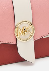 Barevná kabelka s růžovým a červeným designem, vyrobená z texturovaného materiálu, s výrazným zlatým kulatým logo a krémovým popruhem.