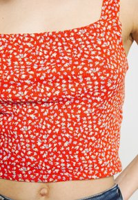 Haut crop rouge à imprimé floral blanc et bleu clair, porté avec un jean en denim bleu, découvrant le ventre et une partie du bras.
