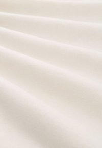 Tissu en coton de couleur crème clair avec une surface lisse et légèrement texturée, présentant des plis et des drapés subtils.