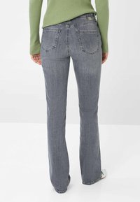 Jeans grigi con vestibilità aderente e gamba a zampa, due tasche posteriori e una toppa in vita tono su tono. Il tessuto ha una finitura liscia e leggermente strutturata.