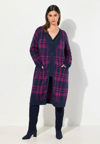 Lång marinblå kofta med rosa rutmönster, öppen fram, två fickor, ribbad mudd, bärs över en marinblå topp och byxor. Slät textur.