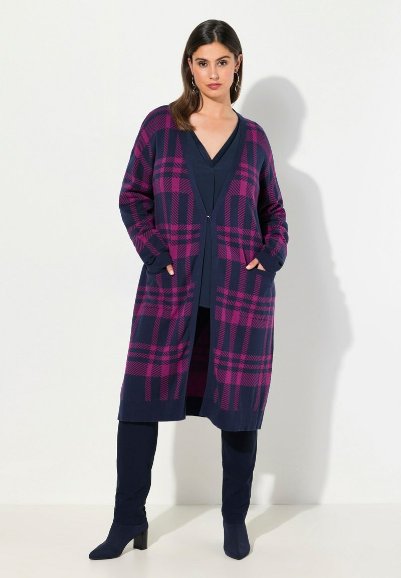 Lång marinblå kofta med rosa rutmönster, öppen fram, två fickor, ribbad mudd, bärs över en marinblå topp och byxor. Slät textur.