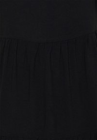 Černá látka se sbíraným švem vytvářejícím jemné, vertikální záhyby a mírně zakřivený horní okraj.