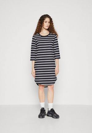 Robe rayée en bleu marine et blanc, à manches trois-quarts, encolure dégagée, ourlet arrondi, portée avec des chaussures noires et des chaussettes blanches.