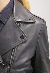 Black leather motorcycle jacket featuring a notched collar, zip closure, and snap buttons, showcasing a smooth texture and tailored fit.