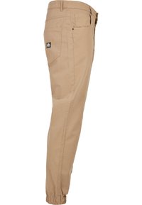 Khaki-housut, joissa on kapeat lahkeet, joustavat hihakujat ja takatasku, jossa on logopläjäys. Valmistettu kevyestä kankaasta.