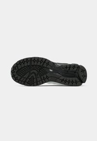 Semelle noire de chaussure de course avec des rainures profondes et des motifs de grip texturés, présentée à plat sur un fond gris clair.