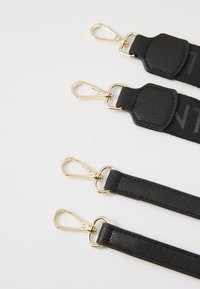 Black straps with gold hardware clips, featuring textured leather and smooth material, arranged in a layered manner, showcasing varying widths.