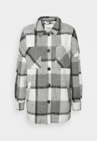 Camicia in flanella a quadri grigia e bianca con due tasche sul petto, bottoni neri e maniche lunghe. Tessuto morbido con una vestibilità rilassata.