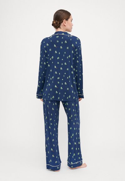 Navy blue pajama set with a tree pattern, made of soft fabric. Long-sleeve top with collar and matching pants featuring cuffed ends.
