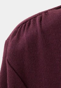 Gros plan d'un tissu tricoté bordeaux montrant l'épaule et l'encolure avec des détails de couture froncée.