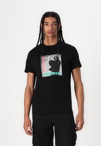 Black cotton t-shirt featuring a graphic print in gray, pink, and turquoise with "WEEKEND OFFENDER" text. Short sleeves, crew neckline.