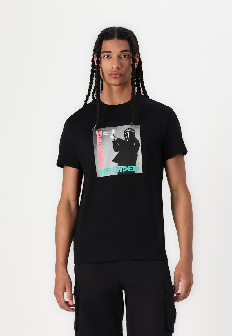 Black cotton t-shirt featuring a graphic print in gray, pink, and turquoise with "WEEKEND OFFENDER" text. Short sleeves, crew neckline.