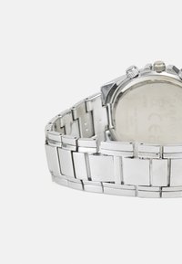 Montre en acier inoxydable argenté avec un design de bracelet à maillons brillant et un boîtier rond. Elle présente un dos lisse et deux couronnes sur le côté.