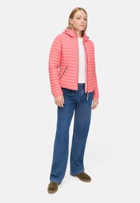 Rosa gepolsterte Jacke mit Kapuze, mit gestepptem Material und Reißverschlüssen, kombiniert mit blauen weitem Bein Jeans und braunen Schuhen.
