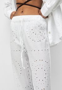 Pantalon en coton blanc agrémenté de broderies ajourées avec des découpes circulaires et ovales, taille élastique et détail de cordon.