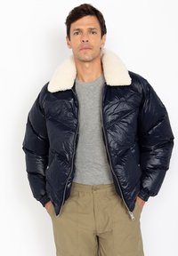 Marine blouson met een nepbont kraag, ritssluiting, elastische manchetten en een glanzende afwerking. Draag het over een grijs T-shirt en khaki broek.