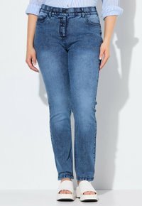 Jeans ajustados de denim azul, con cintura alta, ligero desgastado y un clásico diseño de 5 bolsillos. Combinados con sandalias blancas de plataforma.