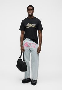 Μαύρο βαμβακερό μπλουζάκι με γραφικό σχέδιο, συνδυασμένο με ανοιχτό μπλε τζιν παντελόνι διακοσμημένο με ροζ εικονογράφηση. Μαύρη τσάντα και σκούρα παπούτσια.