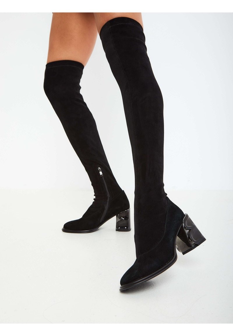 Black over-the-knee boots in soft suede with a pointed toe and textured block heel. Features a side zipper and sleek silhouette.