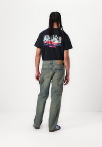 Black cotton t-shirt featuring a colorful graphic print; light blue denim pants with multiple pockets; blue and white striped socks.