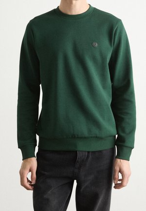 Sweatshirt vert avec un col rond, des poignets et un ourlet côtelés. Présente un petit logo circulaire sur la poitrine gauche. Fabriqué en tissu doux.